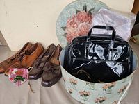 Photo showing two pairs of men's shoes, black patent leather handbag, large floral hat box, and men's shirt in original plastic packaging.