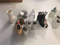 Photo showing the 19 vintage glassware and ceramic decorative pieces including ceramic boots, salt and pepper shakers, and bell-shaped glass item.