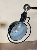 Close-up of black metal desk lamp showing chipped black paint and perforated inner shade