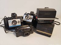 Group of 5 vintage cameras including 2 Polaroid Sun 600 instant cameras and 3 35mm cameras, showing front and top sides with lenses and viewfinders visible