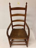 Front view of the rocking chair showing wooden frame, three curved back slats, armrests, and rattan seat.
