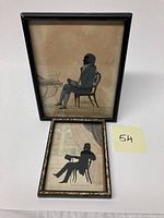 Full view of two framed silhouettes depicting seated Victorian gentlemen with black frames and backing papers, showing overall condition and size.