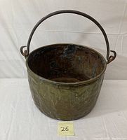 Full view of antique brass and copper pot with cast iron handle against a white background.