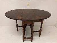 Front view of oval-shaped antique drop leaf gate leg table with all leaves extended, showing turned legs and wooden top.
