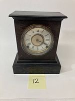 Front view of black cast iron mantle clock showing engraved scroll patterns on the body and base with Roman numeral clock face.