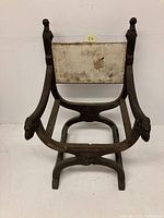 Full view of antique Savonarola chair frame showing carved ram heads at the armrests and worn, missing upholstery.