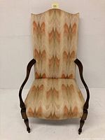 Front view of Martha Washington style upholstered chair with beige and orange patterned fabric and dark wooden frame with curved arms and turned legs.
