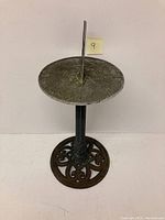 Front view of metal sundial showing the circular dial with raised numbers and the triangular gnomon.