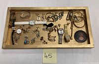 Full view of mixed jewelry items including watches, earrings, bracelets arranged on a wooden tray