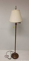 Full view of the floor lamp showing the slim bronze stand, round base, and cream pleated shade.