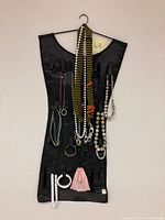 Front view of black Umbra double sided jewelry travel bag shaped like a dress with multiple necklaces, bracelets, and accessories secured in loops.