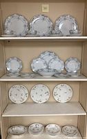 Shelf with various china pieces including blue floral dinner plates, salad plates, bread plates, cups, saucers, and smaller gold floral plates.