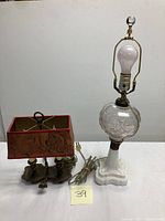 Full view of both lamps on a white surface showing milk glass lamp with crystal globe and brass fixture, and brass lamp with red marbled shade.