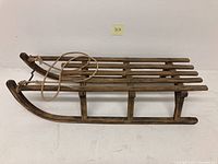 Side angle of the rustic wooden sled showing wooden slats and cast iron runner with rope attachment.