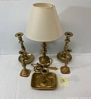 Full view of vintage brass lamp with fabric shade and five different brass candle sticks in front of white backdrop.