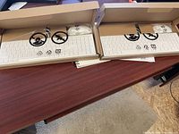 Two white computer keyboards, still in their boxes and original protective plastic, placed on a wooden surface.