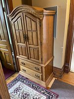 Full view of oak finish armoire with double doors closed, showing overall design, wood grain, and hardware