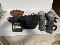 Photo shows the complete lot of baseball equipment arranged on a white surface, including shin pads, chest protector, and gloves.