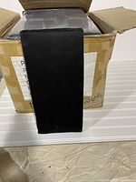 Box containing 14 new black rectangular padded cushions approximately 7 inches by 15 inches each.