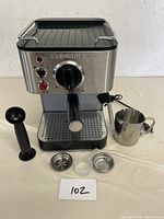 Front view of the Cuisinart espresso maker with tamper, frothing pitcher, two filter baskets displayed on the counter, showing controls and brand name.