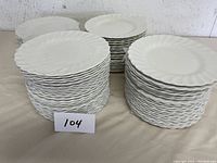 Stacks of three large groups of fine white dessert plates with scalloped edges, approximately 125 plates in total