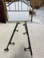 Wooden double bed headboard with metal decorative scrollwork and separate black metal frame rails with wheels.