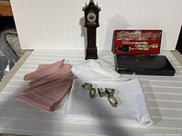 Photo shows set of linens in white and pink, silver napkin rings, miniature wooden grandfather clock, and Royal Sealy gold plated dessert serving set box.