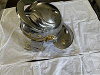 Polished steel Roman helmet with brass rivets and hinged neck guard on white fabric.