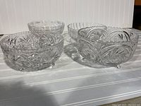 Four crystal and glass bowls with detailed cut patterns, two crystal bowls on feet, displayed on a white surface
