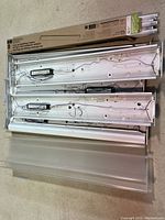 Five white shop light fixtures laid out flat with diffuser covers and fluorescent bulbs visible, showing wiring and ballasts on the backside of some fixtures.