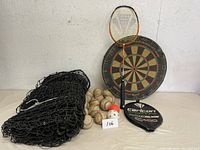 Baseball net with used baseballs, dart board with darts, badminton racket and cover