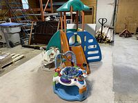 Wide view showing the Little Tikes play centre, toddler activity saucer, and baby swing in a storage setting.