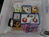 Wide view of costume jewelry lot in original boxes showing necklaces, earrings, watch and bird figurine.