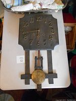 Photo shows full view of dark stained oak wall clock with gold numerals and hands, pendulum visible.