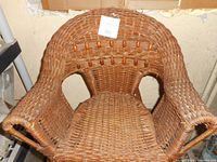 Front angled view of antique child's wicker chair showing woven wicker, curved armrests, rounded backrest, and decorative wooden bead accents.