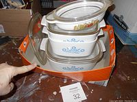 Stack of four white rectangular Corelle casseroles with clear lids, showing blue Cornflower and colorful Spice of Life patterns