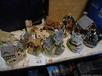 Overview of multiple ceramic houses including thatched roof and stone houses, lighthouse, octagonal harbor building and Christmas chapel.