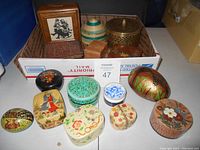 Wide shot showing all small boxes in the lot in a box including wood rectangular, oval, round, and egg-shaped boxes with various handpainted designs and perforated money box