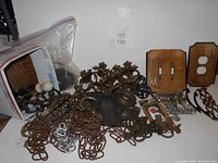 Overview of boxlot contents showing chains, metal handles, wooden knobs, and wooden switchplates on table surface.