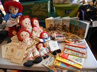 Photo showing a collection of six vintage Raggedy Ann dolls, Beatrix Potter books, and multiple Ladybird books arranged on a table.