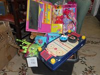 Wide shot of the full toy lot showing Barbie case, Polly Pocket airplane, hockey toy, and other items in black bin