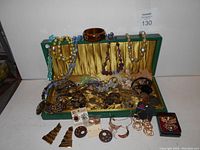 Wide view of green antique cutlery box open and filled with a variety of vintage costume jewelry including necklaces, earrings, bracelets and brooches in multiple colors and styles