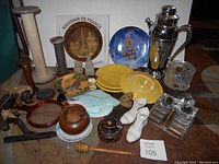 Photo of boxlot showing yellow Fiesta ware plates, blue decorative plate, chrome cocktail shaker, glass inkwell set, antique wooden spools, souvenir plate from France, assorted small figurines, wooden honey dipper, and ceramic fish dish.