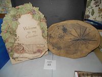 Photo showing both the garden plaque with 'Welcome to my Garden' text and the oval pottery clock with leaf design placed side by side.