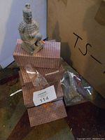 Photo showing a single kneeling Chinese terracotta warrior figurine placed on top of a patterned box along with additional packaged figurines scattered around.