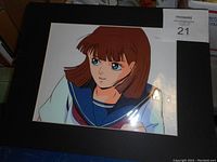 Photo of original animation cel from a Japanese anime showing female character in school uniform under protective cover with authentication label visible.