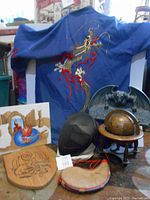 Blue embroidered dragon kimono hanging in background with wooden dragon shield, mesh fencing mask, globe on stand, gargoyle plaque, leather wineskin, artwork print, and cloth cap arranged in front.