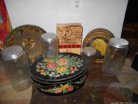 Full view of all canisters and tins arranged on floor showing different shapes, sizes, and lithograph designs including floral and fruit motifs.