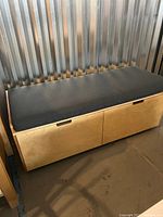 Side view of wooden bench with black cushioned seat and two storage drawers