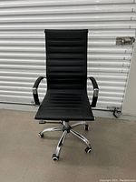 Front view of the black Eames style office chair showing padded ribbed seat and backrest, padded armrests, and chrome five-wheel caster base.
